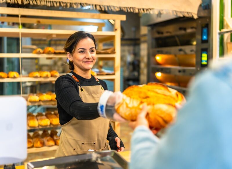 Latin smiling woman selling bread to a client in an artisan bakery